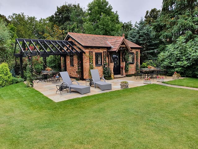 Brick garden room with black timber pergola, sun loungers and sandstone patio on a lawn in a Surrey garden