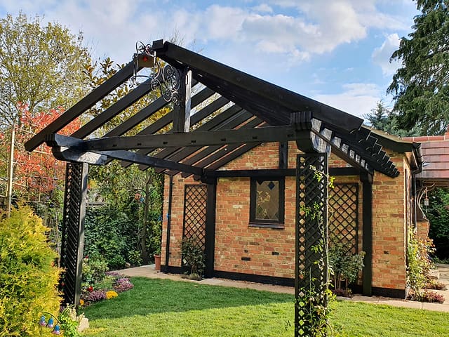 Brick garden room with a black timber pergola and trellis against an autumn blue sky in a Surrey garden