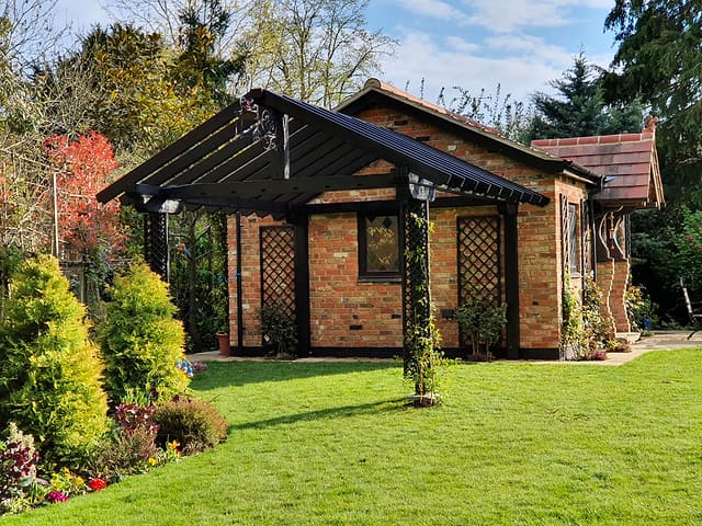 Brick garden room with black timber pergola beside a neatly striped lawn in a Surrey garden