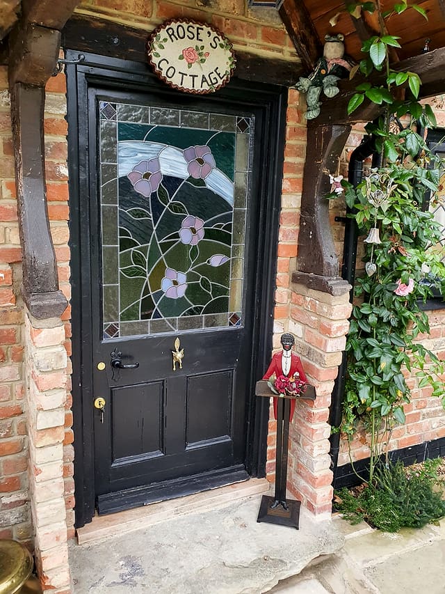 Black panelled front door with a floral stained-glass panel and Rose's Cottage sign on a brick garden room in Surrey