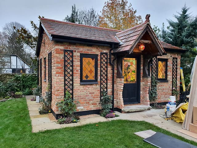 Brick garden room with leaded stained-glass windows and a tiled porch in autumn in a Surrey garden