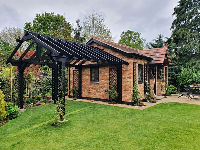 Lush green spring lawn in front of a brick garden room with black timber pergola in a Surrey garden