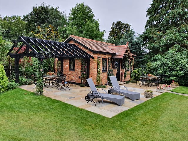 Brick garden room and pergola with sun loungers framed by a neatly mown green lawn in a Surrey garden