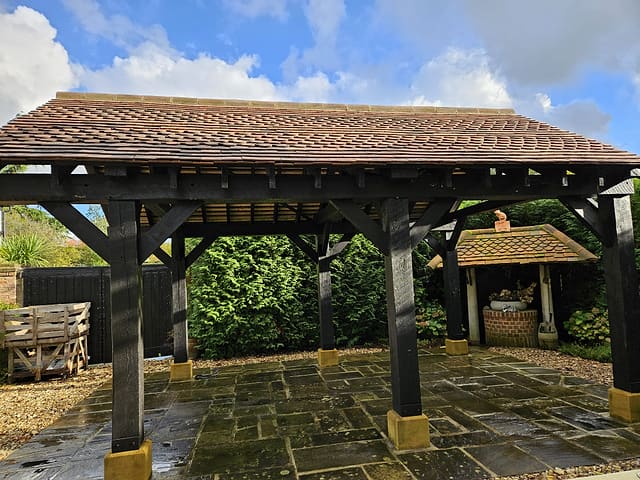 Large green oak gazebo with a clay tiled roof over a flagstone patio under blue sky in a Surrey garden