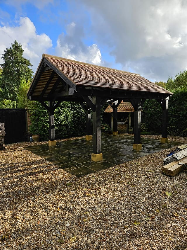 Green oak gazebo with a tiled roof over a flagstone patio with gravel surround in a Surrey garden