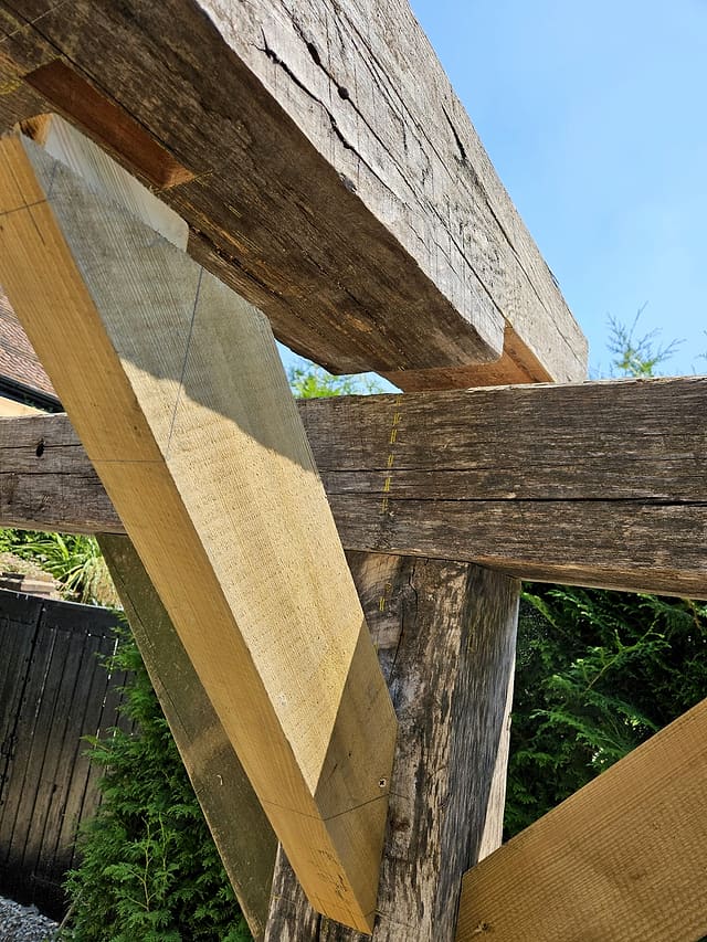 Close-up of a green oak post-to-beam carpentry joint against a blue sky in a Surrey garden